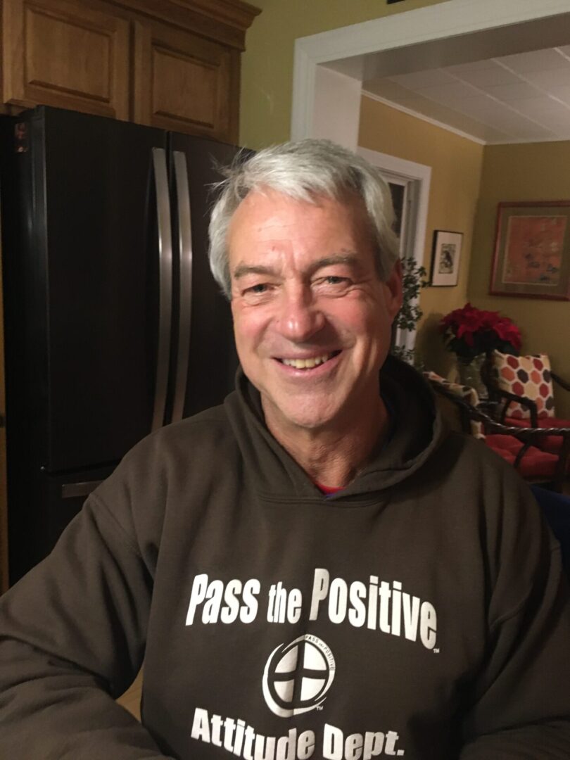 Man smiling in brown hoodie, "Pass the Positive"