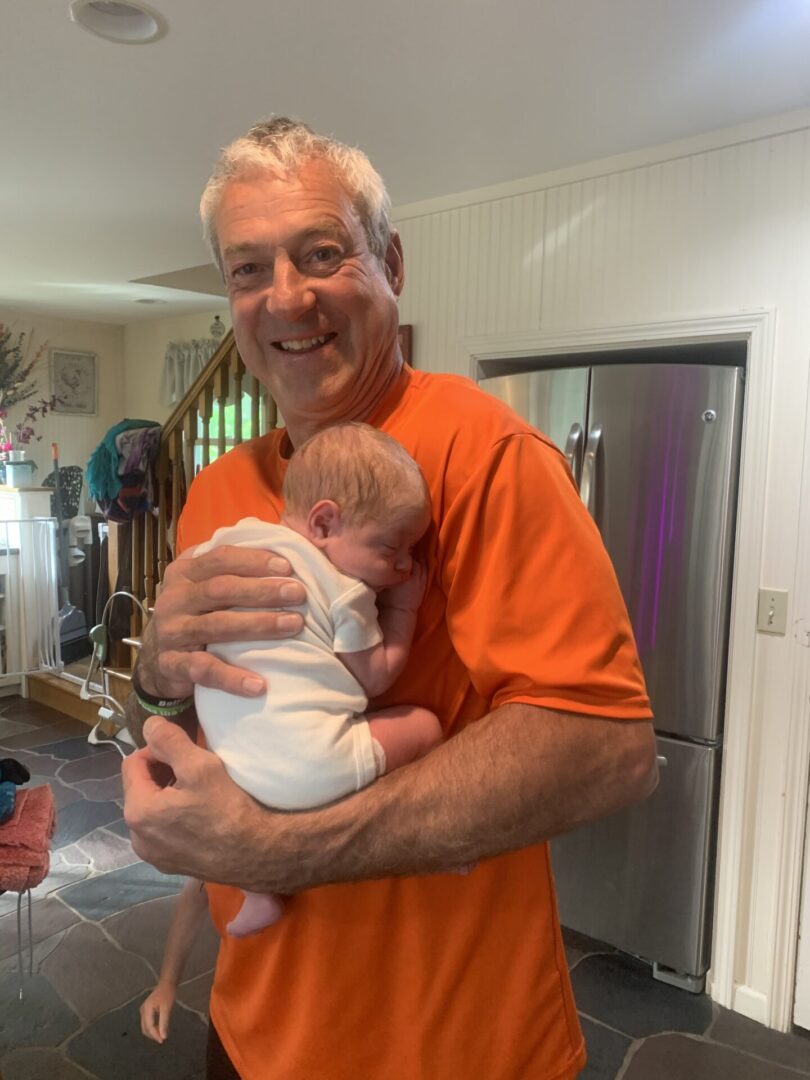 Man in orange shirt holding a baby.